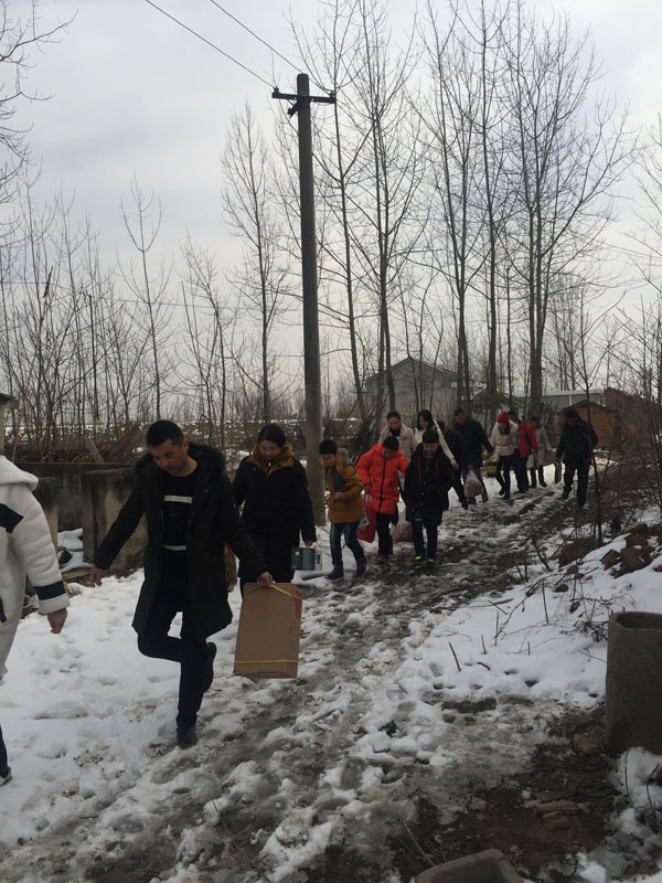 商會愛心慰問團團友正帶著尉問物品，踏著泥雪，迎著寒風，步入村道、前往慰問家庭