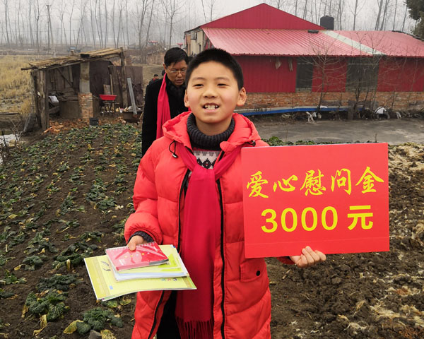 商會慰問團小成員王睿手舉慰問金KT板和自帶的慰問寫字練習本，正懷著贈人玫瑰手留余香的感恩之心，快步走向特困戶家中